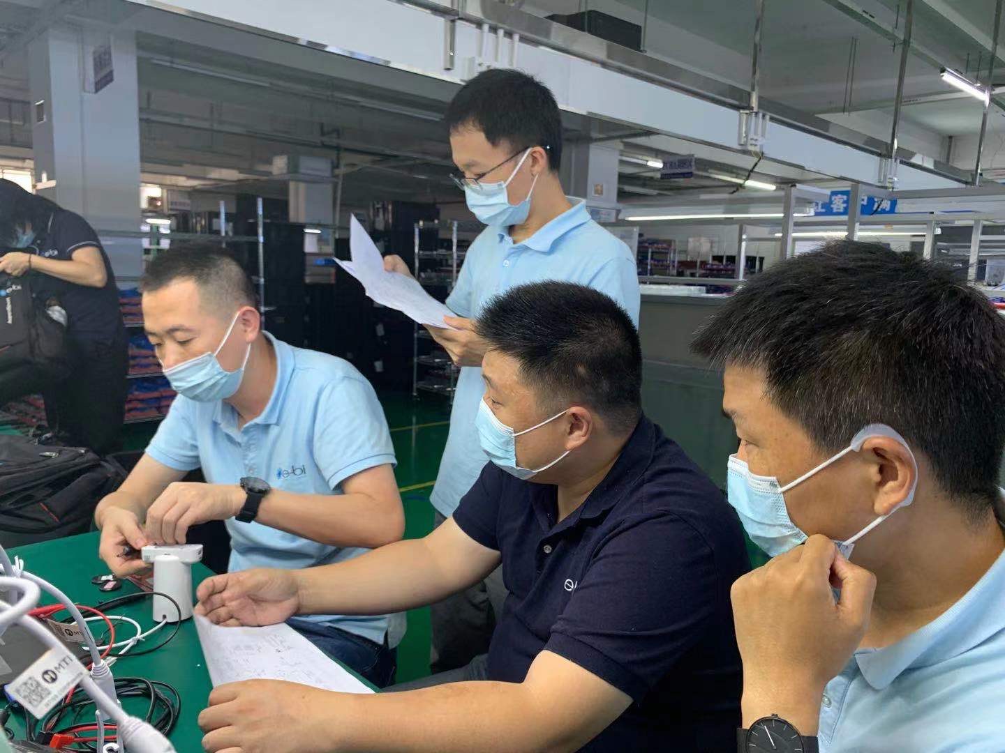 Factory workers wearing face masks while operating machinery, reflecting COVID-19 safety protocols in manufacturing.